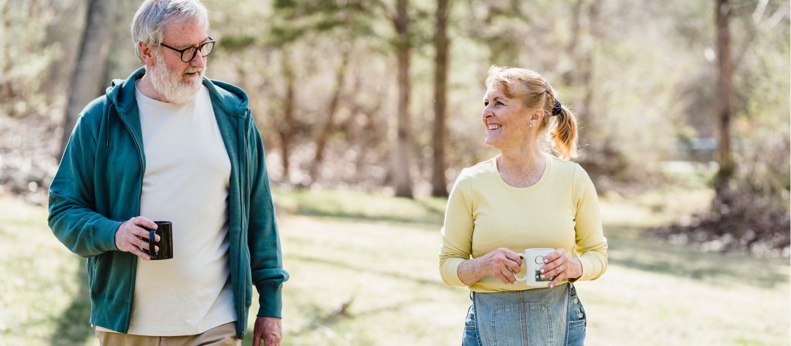 senior couple walking outdoors together both holding coffee cups and looking at each other