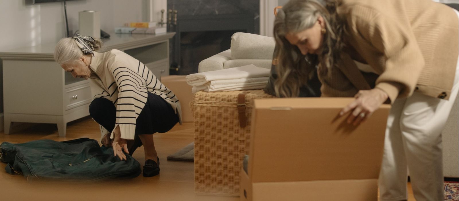 Two women packing boxes in a living room