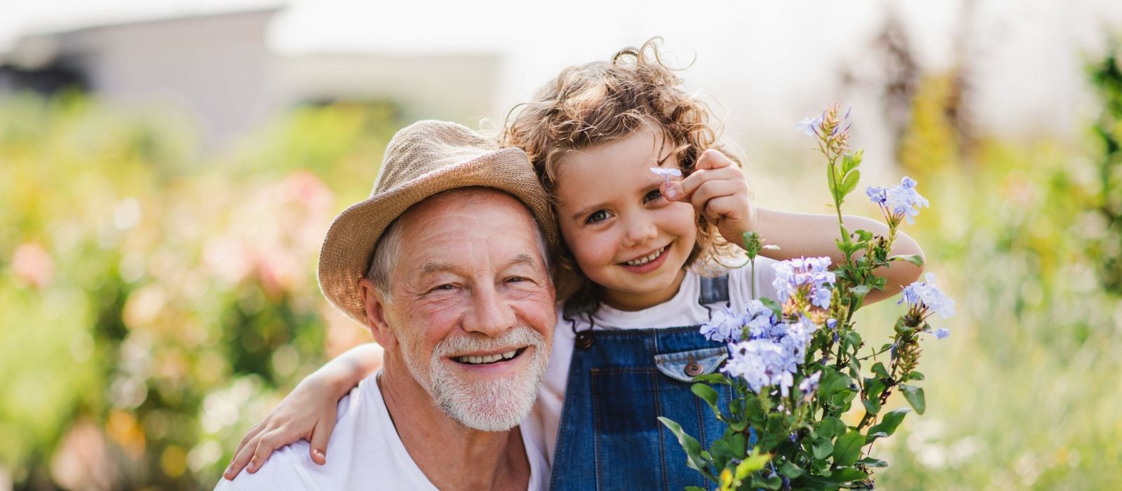 Portrait of small girl with senior grandfather in the backyard garden, standing and looking at camera.