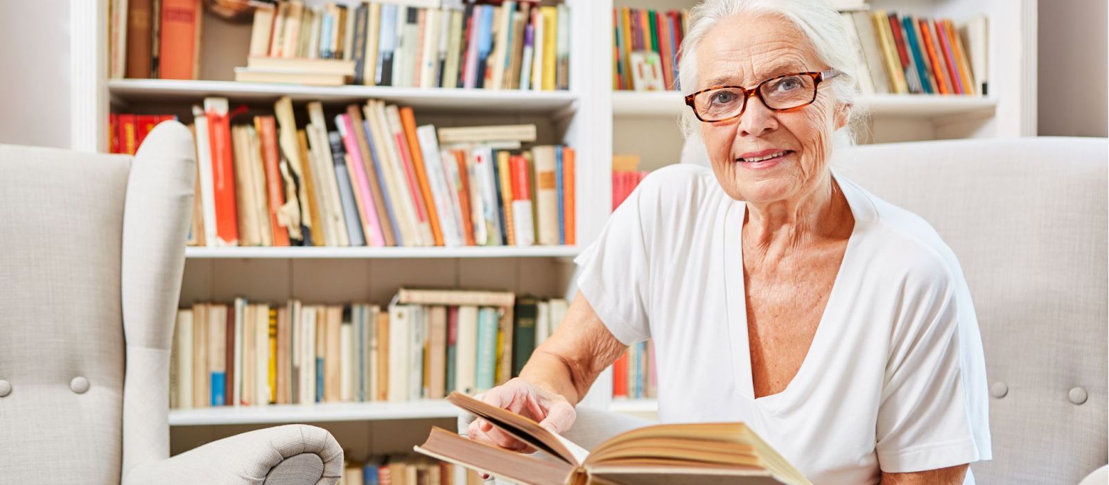 Senior woman with bookshelf in the background reading a book