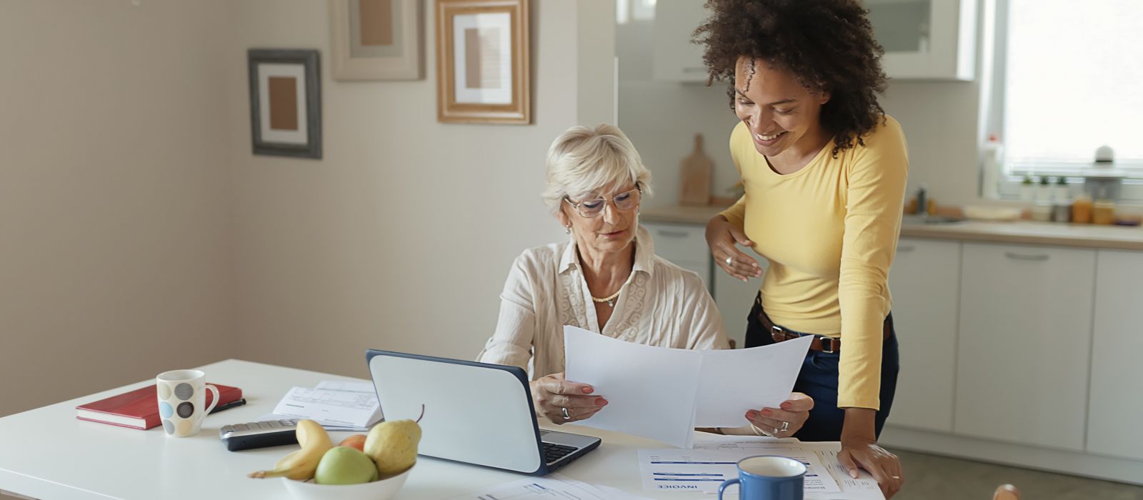 Older woman and younger woman looking at documents and laptop.