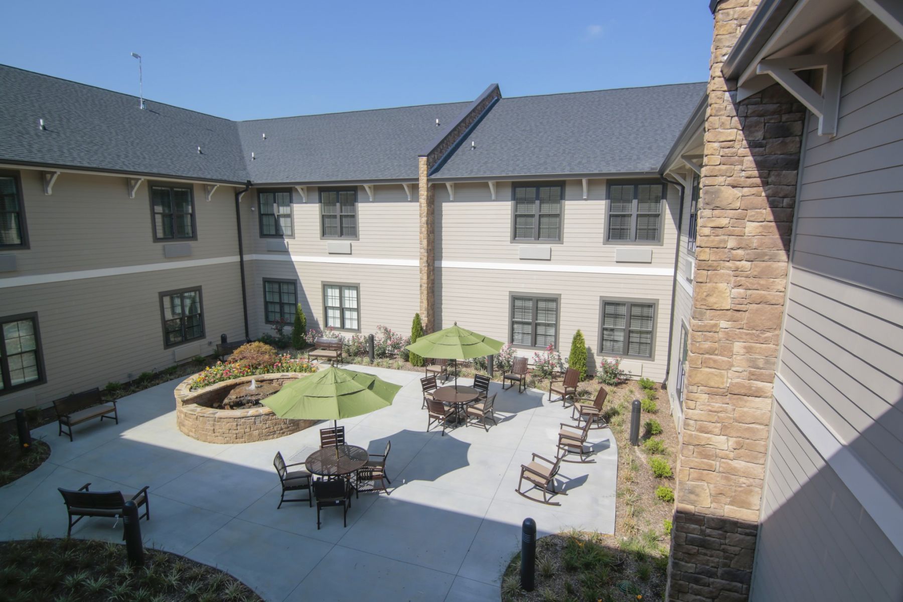 Brickmont at Acworth senior living community outdoor courtyard patio with water fountain, gardens, tables, chairs, and umbrellas