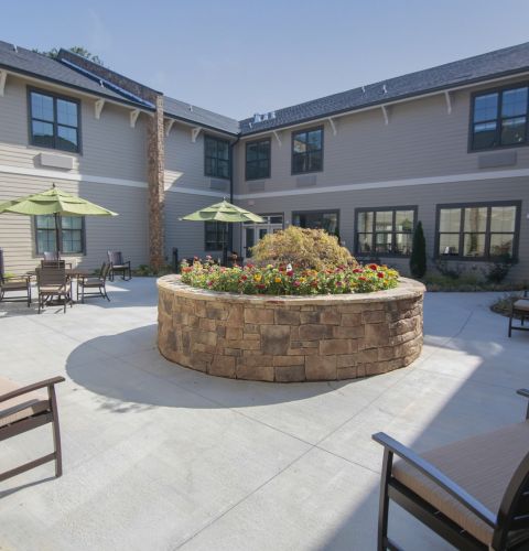 Brickmont at Acworth senior living community outdoor courtyard patio with water fountain, gardens, tables, chairs, and umbrellas