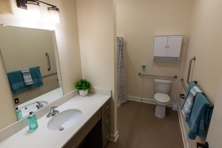 Brickmont at John's Creek senior living community apartment bathroom with accessible sink, toilet, shower, and ample storage