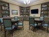 Brickmont at Johns Creek senior living community common sitting area with tables and chairs, tv, bookshelves with decorations, and cabinets of games