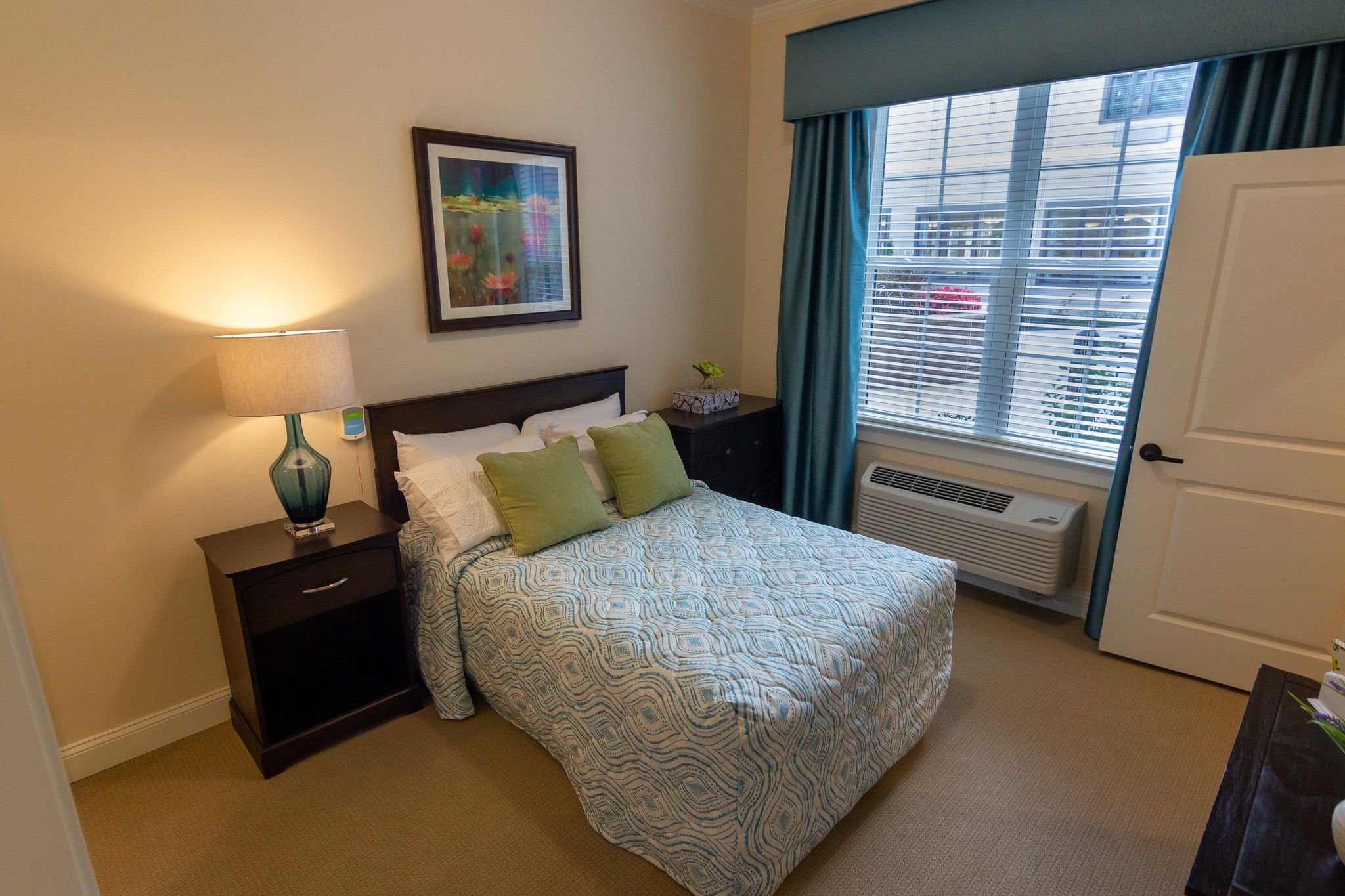 Brickmont at Johns Creek senior living community apartment bedroom with full sized bed, carpeting, and large windows