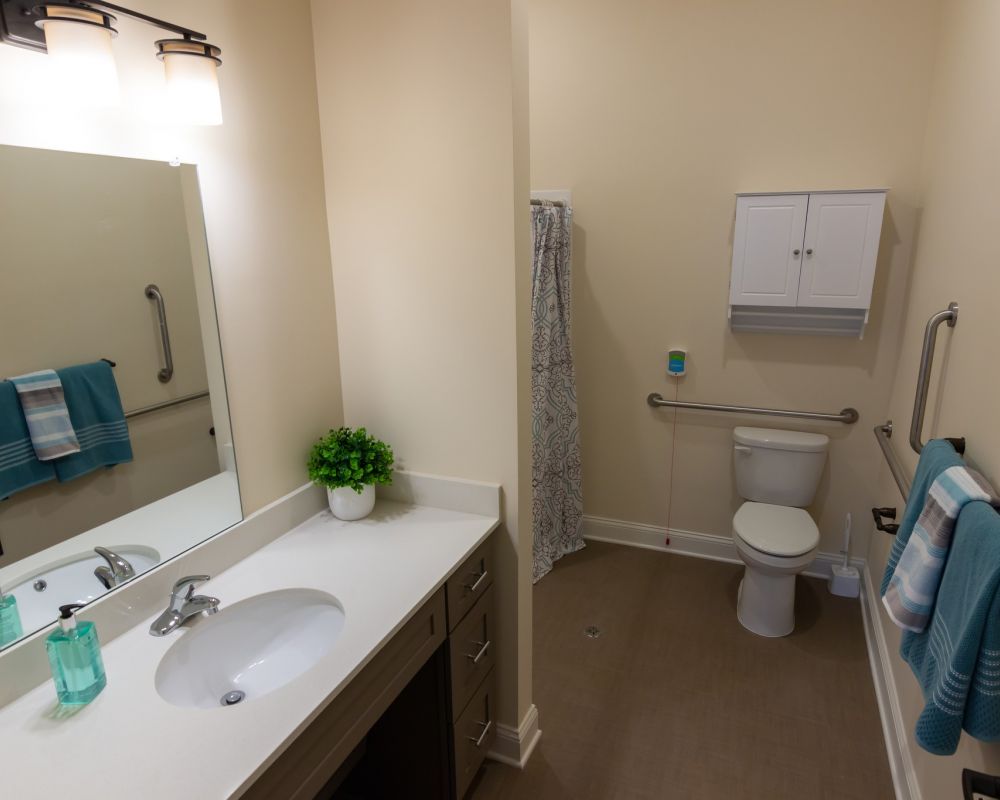 Brickmont at John's Creek senior living community apartment bathroom with accessible sink, toilet, shower, and ample storage