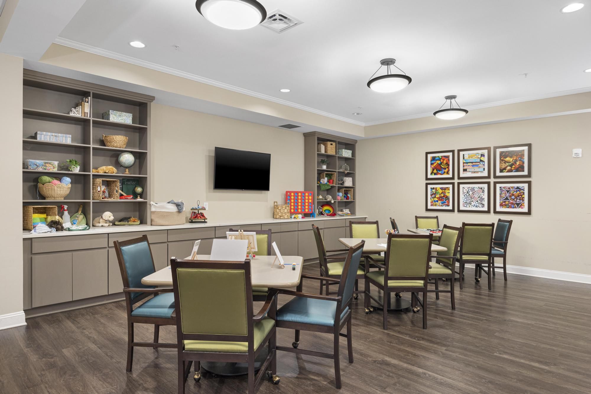 Brickmont at Johns Creek senior living community common sitting area with tables and chairs, tv, bookshelves with decorations, and cabinets of games