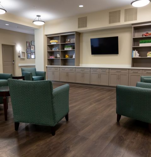 Brickmont at Johns Creek senior living community resident lounge amenity with tables, lounge chairs, games, decorative bookshelves, and flat screen tv