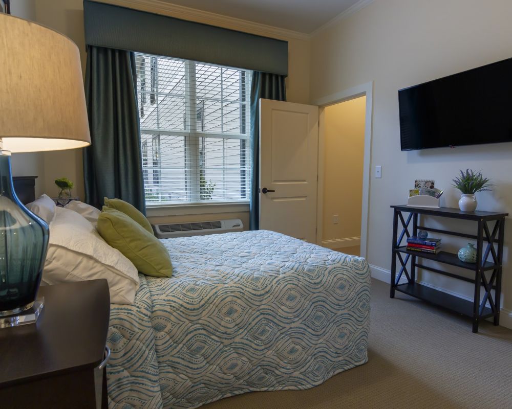 Brickmont at John's Creek senior living community apartment bedroom with full sized bed, carpeting, and large windows