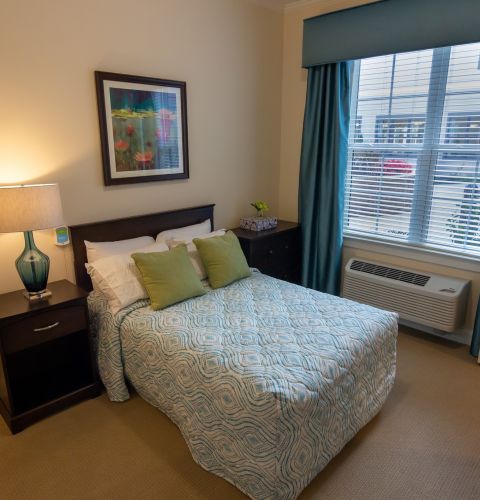 Brickmont at Johns Creek senior living community apartment bedroom with full sized bed, carpeting, and large windows