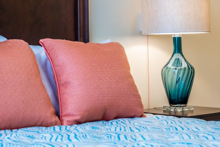 colorful pillows and blankets on a bed next to a pretty lamp and table