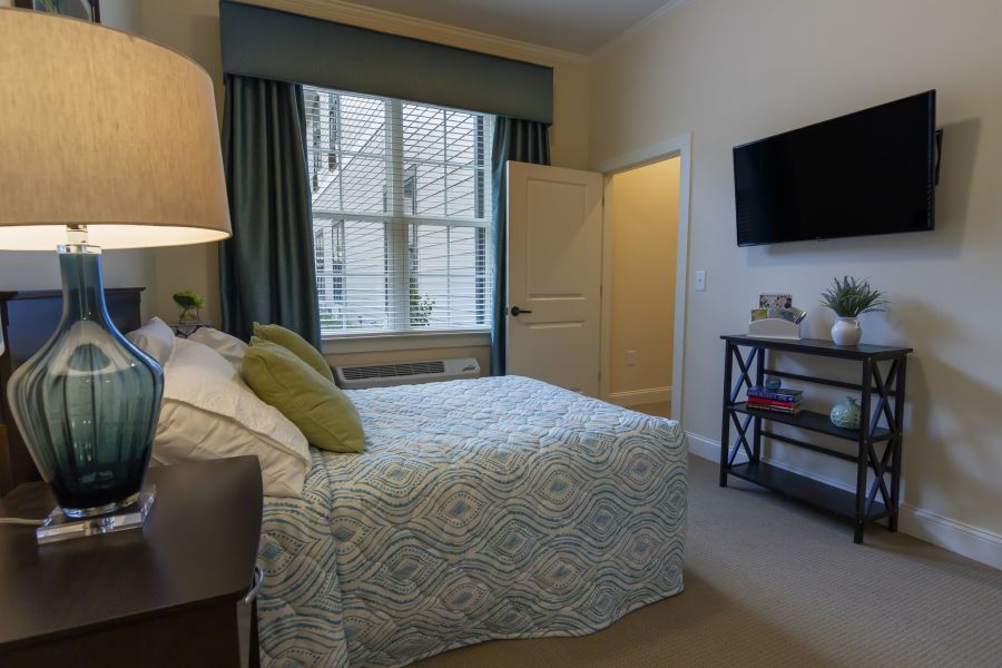 Brickmont at John's Creek senior living community apartment bedroom with full sized bed, carpeting, and large windows