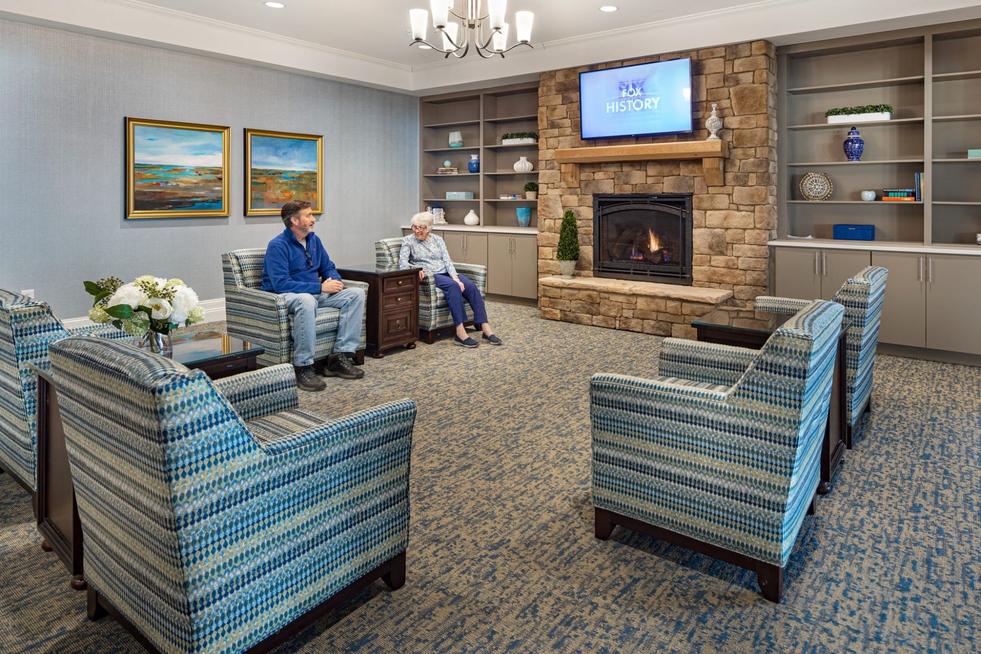 common sitting area with lounge chairs, tvs, bookshelves, and a fireplace