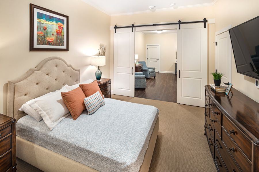 Brickmont at Roswell apartment bedroom with full sized bed, carpeting, and sliding barn doors to main living space
