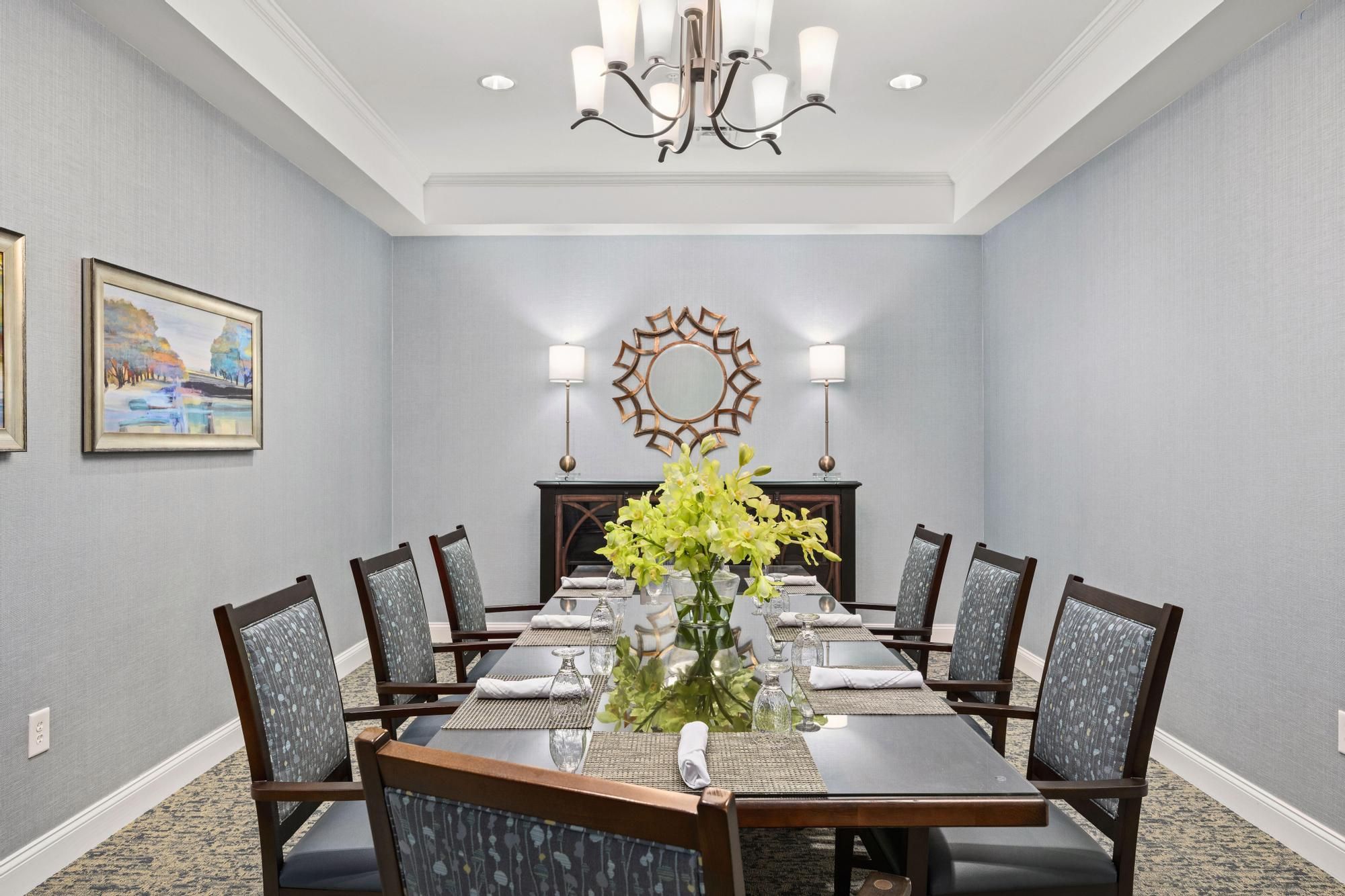 A spacious dining room with green chairs, set tables, and a stone fireplace, lit by large ceiling lights.