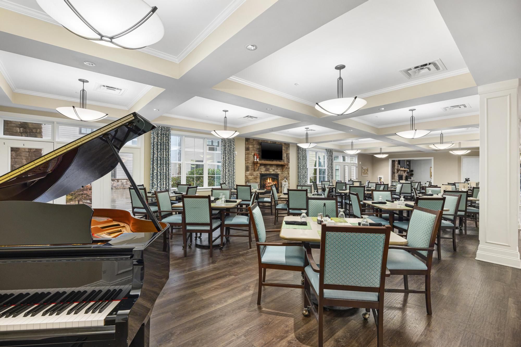 Spacious dining room with a grand piano, elegant lighting, and neatly arranged tables and chairs.