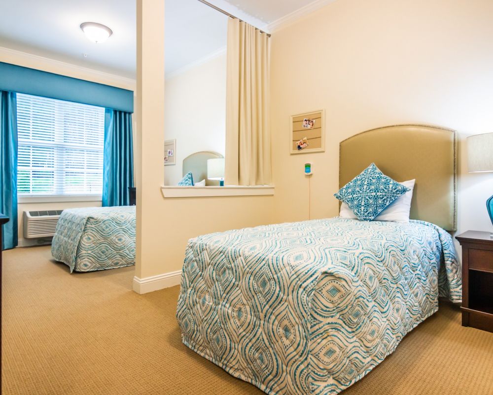 spacious shared apartment bedroom furnished with two beds, carpeting, and a large window