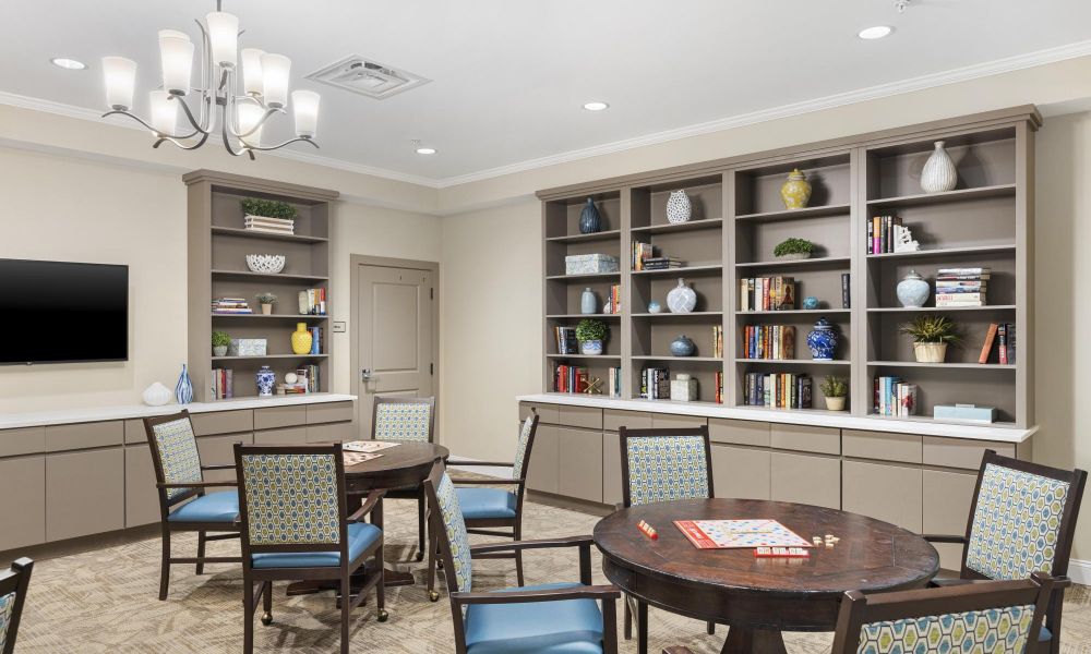 Brickmont at Woodstock resident activity lounge amenity with tables, chairs, large windows, and a flat screen tv