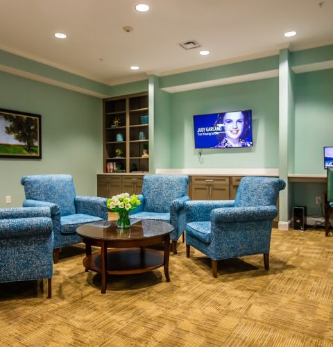 Brickmont at Woodstock  common sitting area with lounge chairs, tvs, bookshelves, and a computer station