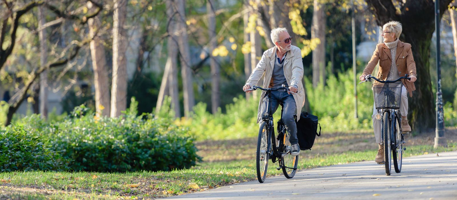 Active senior couple riding bicycles through a paved park path