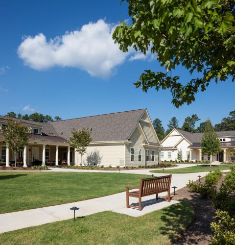 Camellia Place Camellia Place sunny courtyard with a wooden bench, sidewalks, green lawns, and light-colored residential buildings.