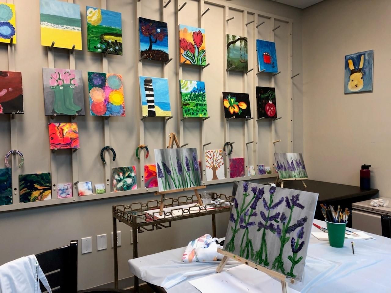 Camellia Place Art studio with colorful paintings on the wall and easels displaying lavender flower paintings on tables.