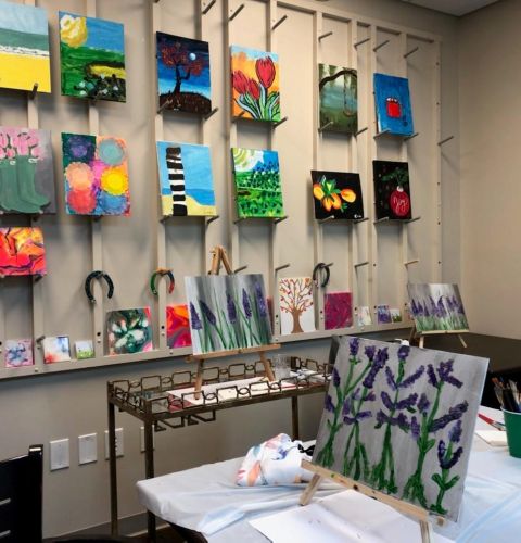 Camellia Place Art studio with colorful paintings on the wall and easels displaying lavender flower paintings on tables.