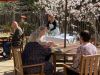 Camellia Place Four older adults sit at patio tables under umbrellas; a woman stands at a serving table in the background.