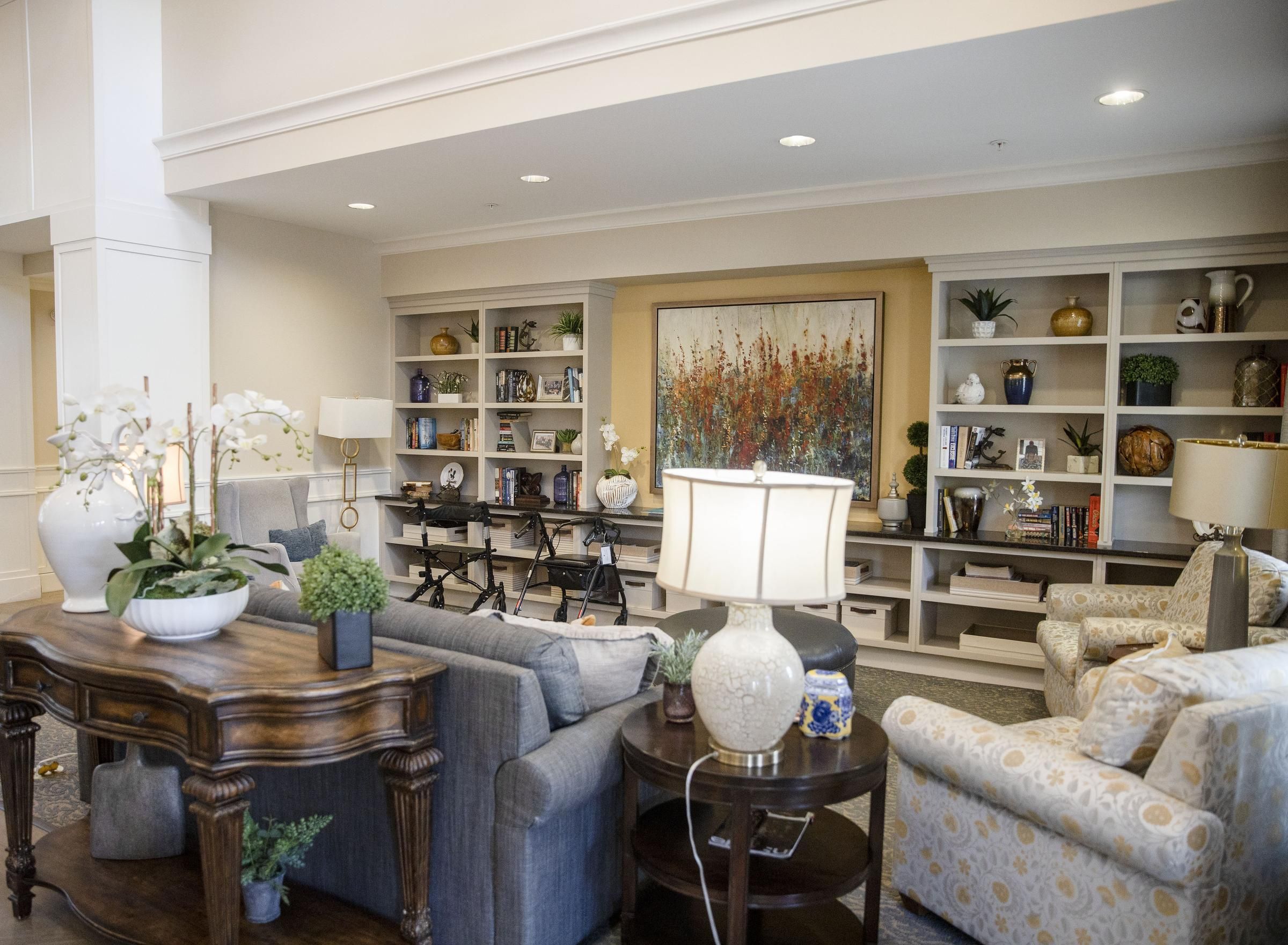 Camellia Place Camellia Place A cozy living room with sofas, armchairs, lamps, plants, and built-in shelves filled with books and decor.