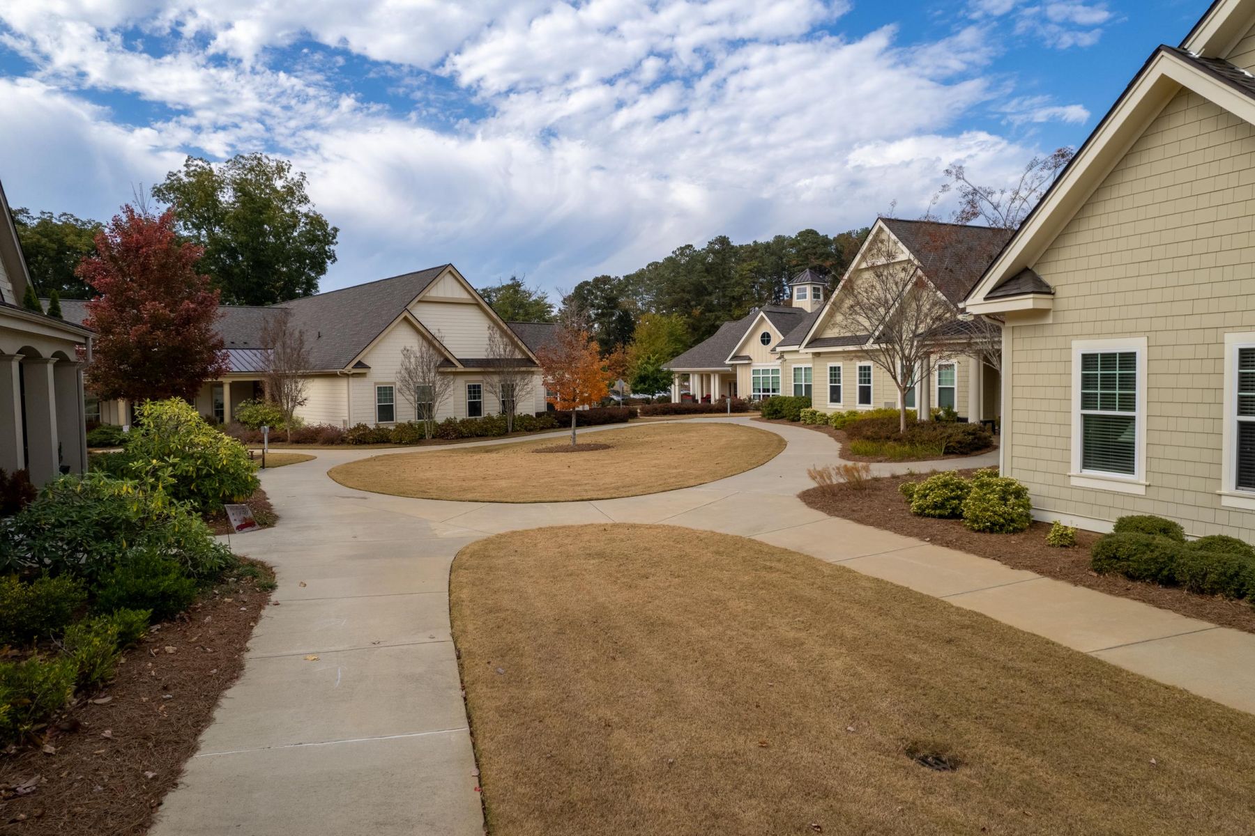Camellia Place A curved sidewalk winds through a quiet neighborhood with well-kept lawns and cottage-style homes under a blue sky.