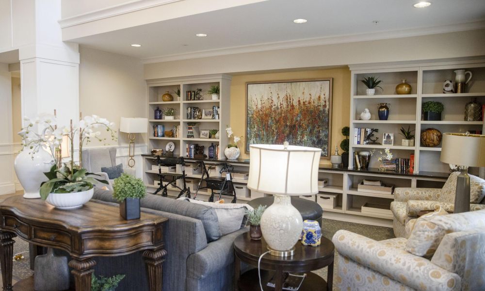 Camellia Place A cozy living room with sofas, armchairs, lamps, plants, and built-in shelves filled with books and decor.