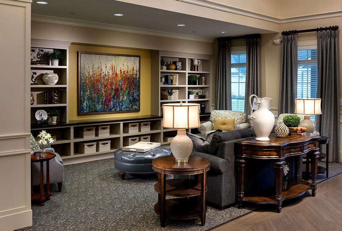 Camellia Place Elegant living room with gray sofa, lamps, art, shelves, and decorative items in a cozy, well-lit setting.