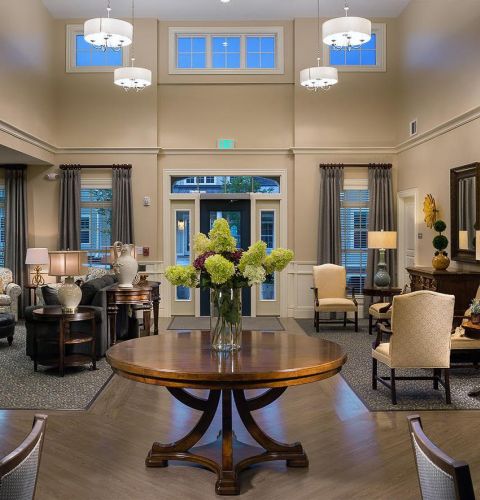 Camellia Place Elegant, well-lit lounge with a round table, floral centerpiece, sofas, chairs, lamps, and large windows.