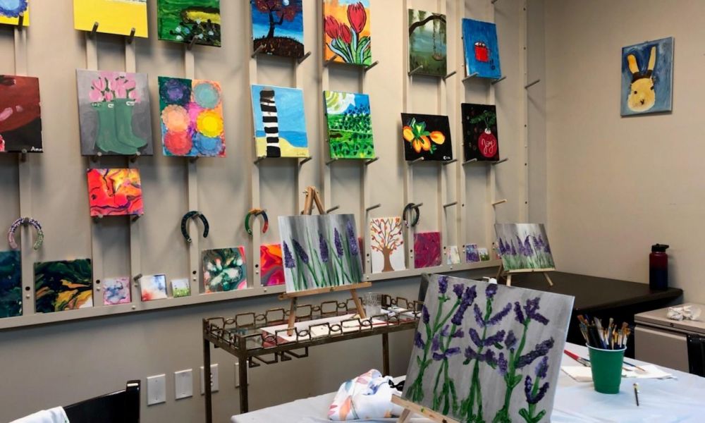 Camellia Place Art studio with colorful paintings on the wall and easels displaying lavender flower paintings on tables.