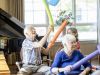 Camellia Place Seniors play with colorful foam noodles and balloons while seated indoors near a piano.