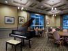 Camellia Place A grand piano in an elegant room with round tables, chairs, framed art, and large windows.