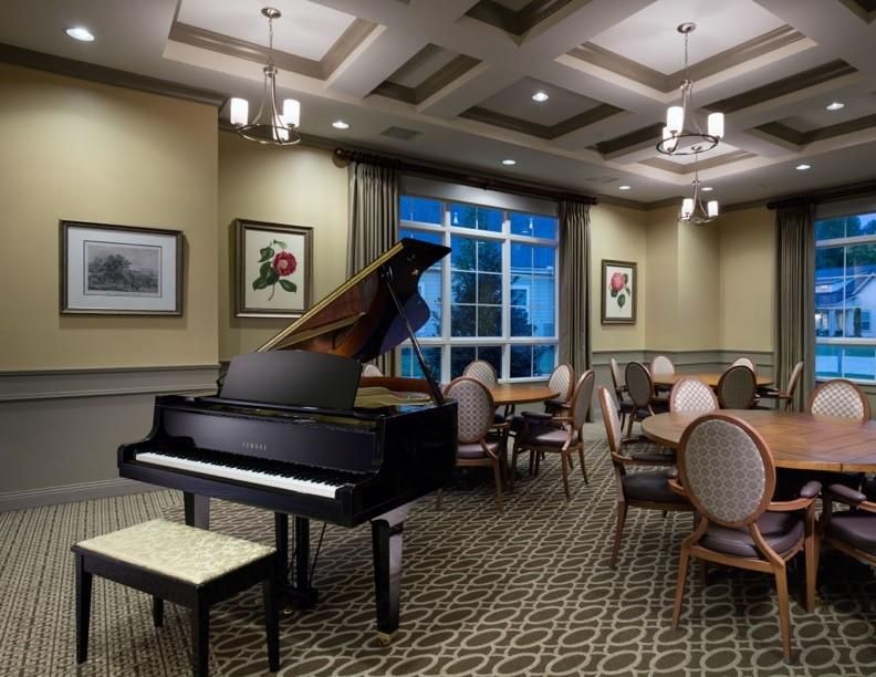 Camellia Place A grand piano in an elegant room with round tables, chairs, framed art, and large windows.