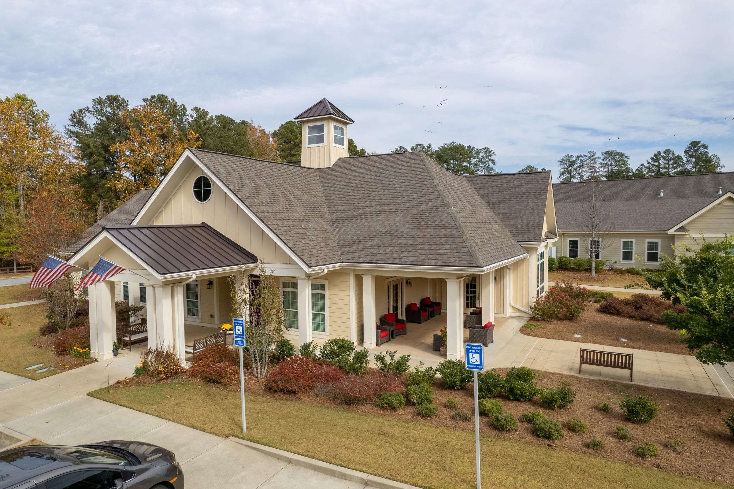 Camellia Place One-story building with a front porch, American flags, benches, and accessible parking spaces.