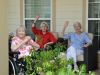 Camellia Place Three elderly women sitting outdoors, two of them waving and smiling, with plants in the foreground.