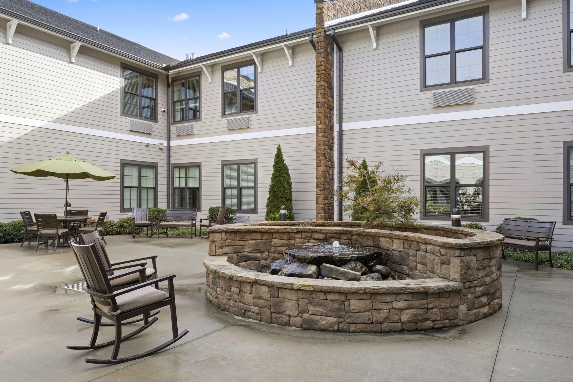 The Claiborne at Acworth senior living community outdoor courtyard patio with water fountain, gardens, tables, chairs, and umbrellas