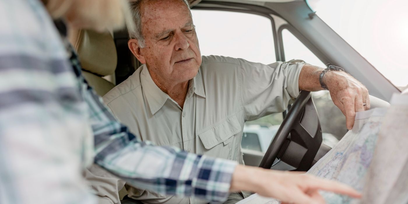 An older man and woman sit in a vehicle, looking closely at a paper map and discussing directions.