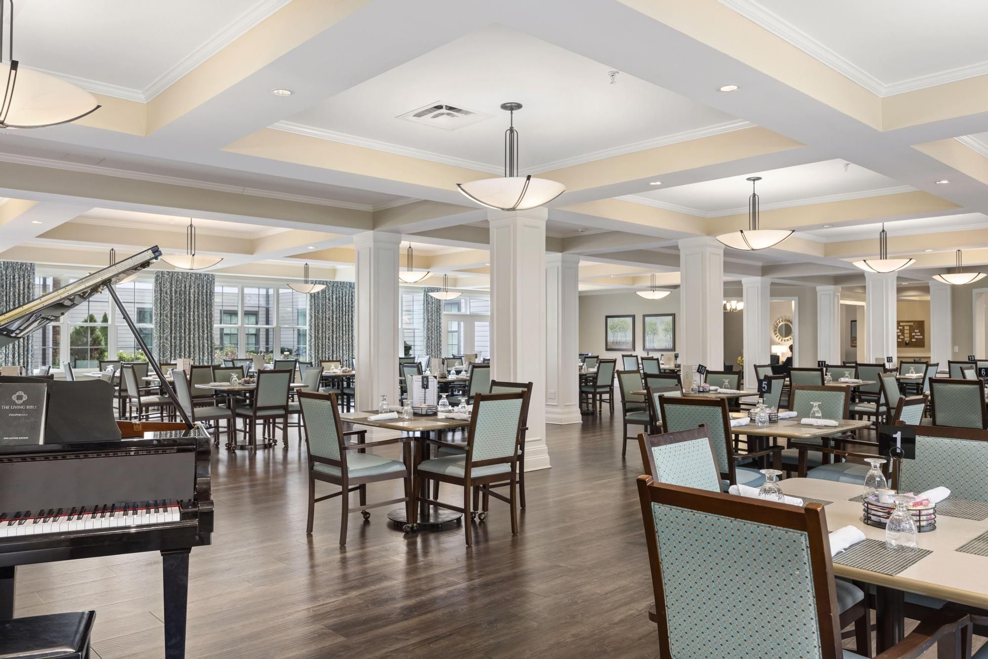 The Claiborne at Acworth resident dining room amenity with tables and chairs, a stone fireplace, and grand piano