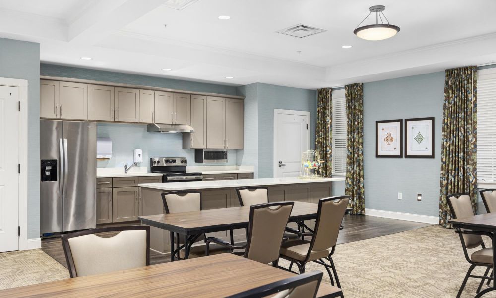 The Claiborne at Johns CreekBrickmont at John's Creek senior living community memory care dining area and activity space with kitchen, tables, chairs, and large windows