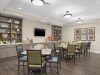 The Claiborne at Johns Creek senior living community common sitting area with tables and chairs, tv, bookshelves with decorations, and cabinets of games
