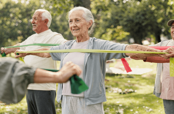 Seniors exercising outdoors with resistance bands, smiling and standing in a park.