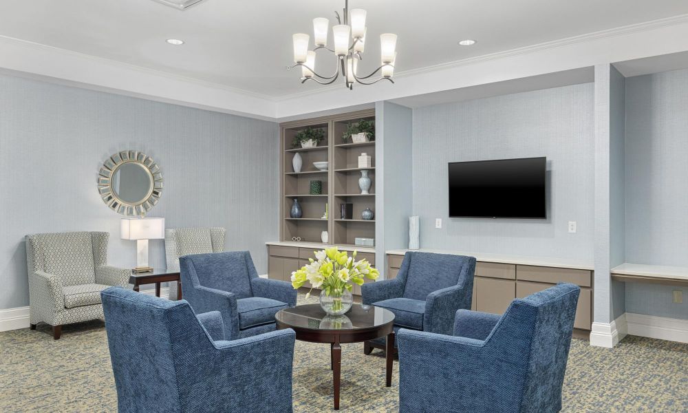 The Claiborne at Johns Creeksenior living community resident lounge amenity with tables, lounge chairs, games, decorative bookshelves, and flat screen tv