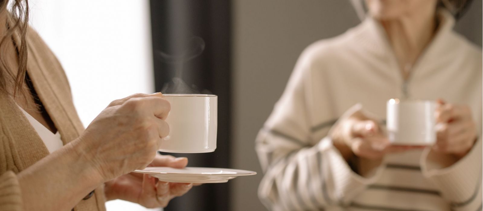 Women drinking hot beverages in white mugs.