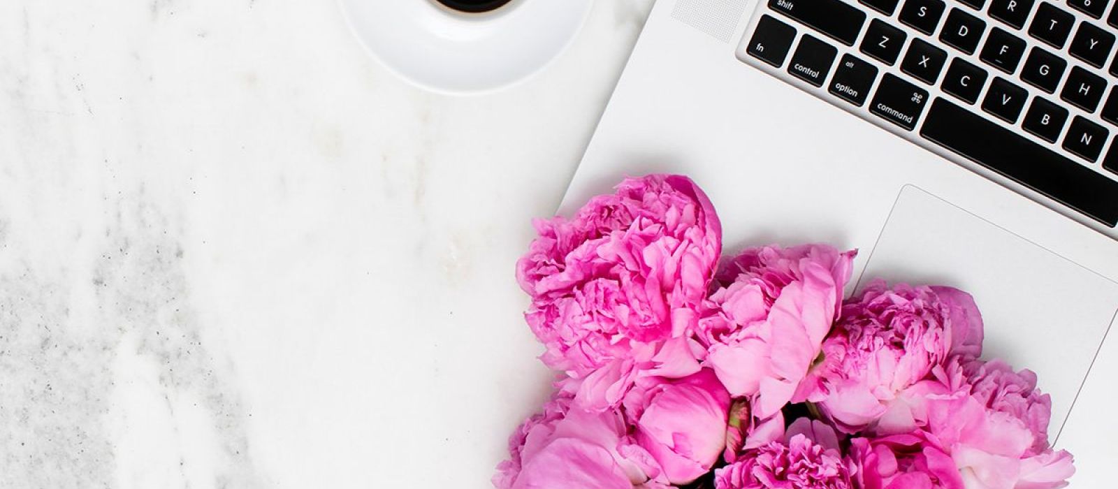 coffee and computer on marble desk with pink flowers