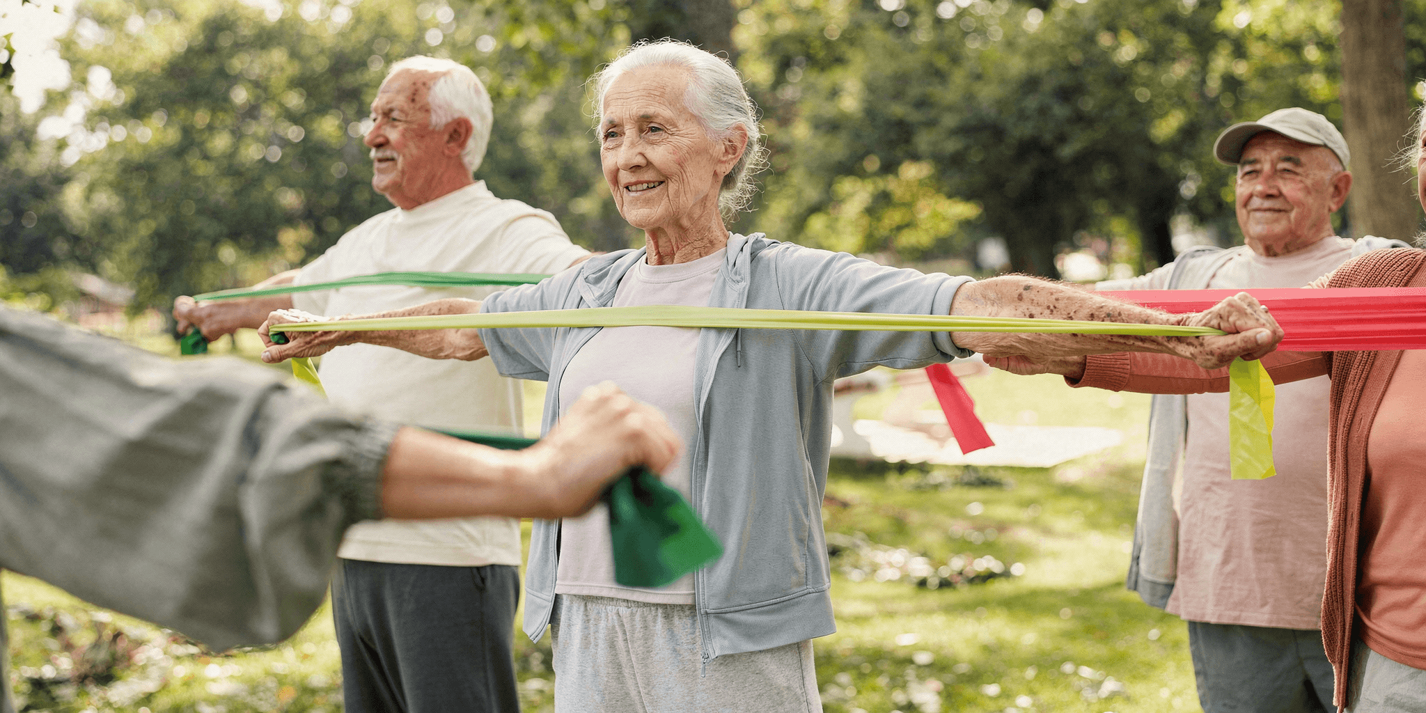 Seniors exercising outdoors with resistance bands, smiling and standing in a park.